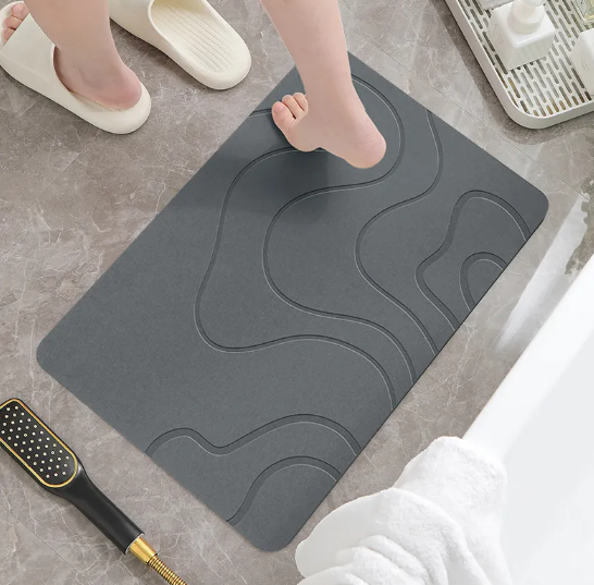 Wet foot stepping onto a dark grey diatomite bath mat that absorbs water instantly